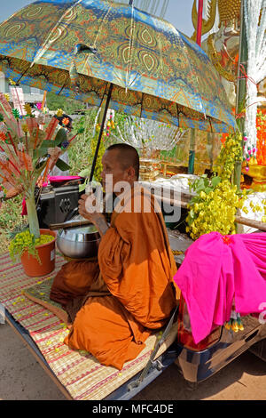 Thailändischen buddhistischen Mönch mit Regenschirm in der Sonne, während eine auf Bambus Matte auf der Rückseite eines Lkw, songkran Tag 13. April 2018 im Isaan, Thailand sitzt Stockfoto