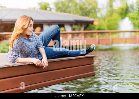 Junge Frau Erholung und Spaß im Park sitzen auf einem Steg über den See Stockfoto