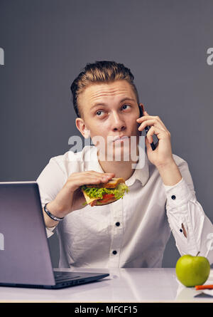 Man Hamburger im Büro Essen, während Anruf auf seinem Handy Stockfoto