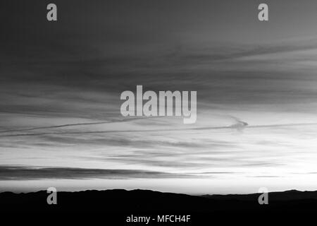 Sonnenuntergang über die Berge in der Ferne, mit tiefen Himmel voller Wolken und Kondensstreifen Stockfoto