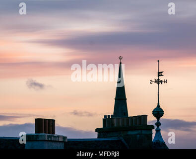 Leith, Edinburgh, Schottland, Großbritannien, 25. April 2018. Wetter in Großbritannien: Farbenfroher Sonnenuntergang über Dächern in Leith. Blick auf Kamintöpfe, Kirchenspitze und Weathervane gegen einen rosafarbenen orangefarbenen Dämmerhimmel Stockfoto