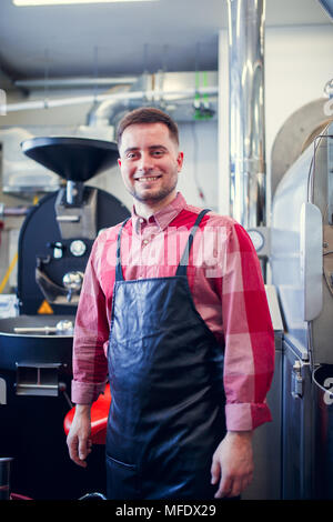 Foto der jungen Brunet in Schürze auf dem Hintergrund der industriellen Kaffeemühle Stockfoto