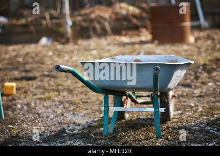 Leere Garten Trolley, Schubkarre. Alte Metall Trolley auf trockenem Gras. Frühling im Garten. Frühling Saison. Reinigung der Garten, Park. Vorbereitung der Garten zum Pflanzen. Cope Raum Stockfoto