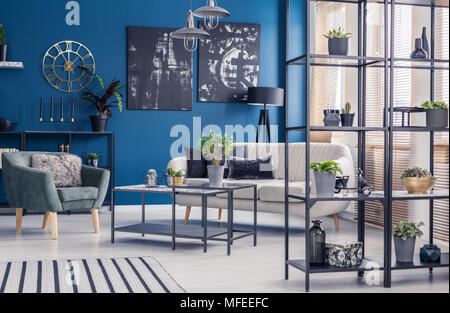 Pflanzen auf Regalen in marine blau Wohnzimmer Einrichtung mit grünen Sessel und beige Sofa Stockfoto