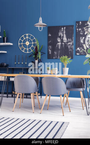 Schwarze Gemälde auf blauen Wand mit gold Uhr in dem modernen Speisesaal Interieur mit grauen Stühlen am Tisch Stockfoto