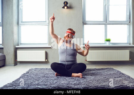 Eine lustige Fetten bärtigen Mann in der Kopfhörer funktioniert Yoga im Zimmer. Stockfoto