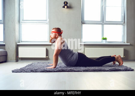 Eine lustige Fetten bärtigen Mann im Sport Kleidung Yoga im Zimmer. Stockfoto