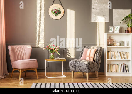 Grau und Rosa Sessel in femininen Wohnzimmer Interieur mit roten Blumen auf hölzernen Tisch Stockfoto