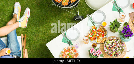 Essen auf den Tisch und Mann hält einen Drink - Grill Party von oben Stockfoto