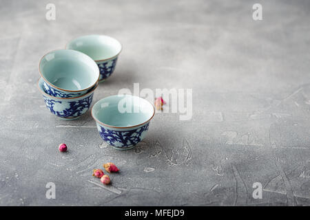 Leere chinesischer Tee Tassen mit einem blauen Muster und trocken Knospen der Rosen auf grauem Hintergrund Stockfoto