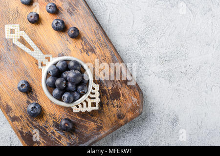 Blaubeeren oder Heidelbeeren in einem antiken Teesieb auf Holzbrett auf grauem Hintergrund. Lecker saftig frische organische Beeren. Gesunde Ernährung und Mutter Stockfoto