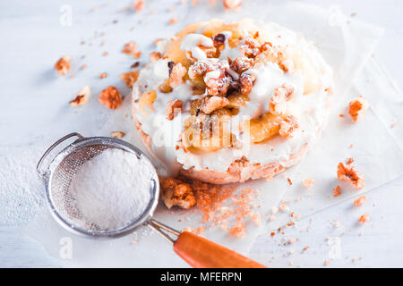 Knäckebrot mit karamellisierten Bananen, Frischkäse, griechischer Joghurt und Walnüsse. Gesundes Frühstück Konzept in einer High Key. Stockfoto