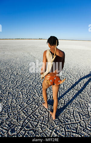 Bushman gekleidet in traditionelle Skins zu Fuß über die Makgadikgadi Pans, bewaffnet mit handgefertigten Jagd Bug getrocknet. Botswana. Modelle freigegeben. Datum: 18.1 Stockfoto