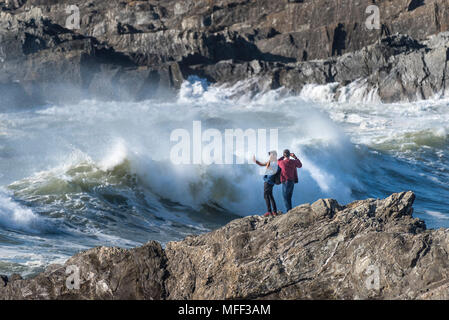 Touristen stehen auf Felsen die Fotografie als große mächtige Wellen brechen am Ufer an wenig Fistral in Newquay Cornwall. Stockfoto