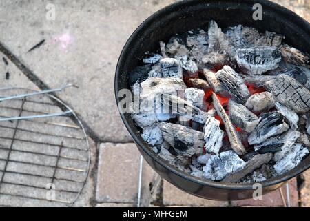 Ansicht von oben auf Holzkohle, weiß-graue Farbe. Die orangefarbene Farbe der brennenden Kohlen am Boden eines Grills. Grill und auf den Gartenfliesen. Stockfoto