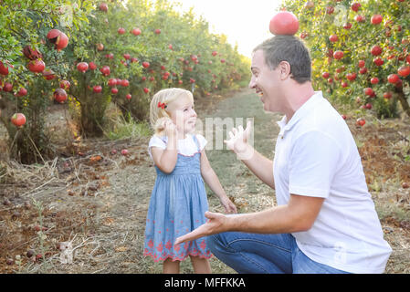 Portrait von Glücklich lächelnde und Laughting Vater mit niedlichen Baby Tochter Spaß in der pomegrate Obst Garten. Ernte, Familienurlaub Konzept. Sun Stockfoto