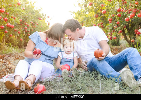 Portrait von Glücklich lächelnde und Laughting Eltern mit niedlichen Baby Tochter Spaß in der pomegrate Obst Garten. Ernte, Familienurlaub Konzept. Su Stockfoto