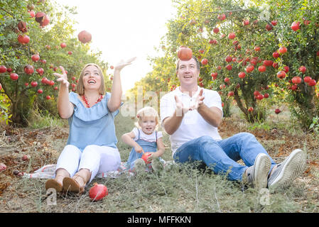Portrait von Glücklich lächelnde und Laughting Eltern mit niedlichen Baby Tochter Spaß in der pomegrate Obst Garten. Ernte, Familienurlaub Konzept. Su Stockfoto