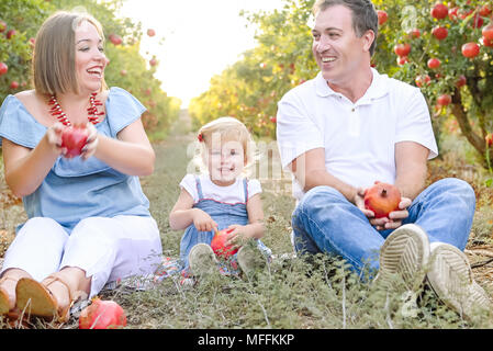 Portrait von Glücklich lächelnde und Laughting Eltern mit niedlichen Baby Tochter Spaß in der pomegrate Obst Garten. Ernte, Familienurlaub Konzept. Su Stockfoto
