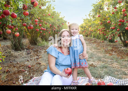 Portrait von Glücklich lächelnde und Laughting Mutter ihre niedlichen Baby Tochter Rest in der pomegrate Obst Garten umfasst. Ernte, Familienurlaub co Stockfoto