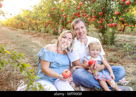 Portrait von lächelnden Eltern mit Baby Mädchen Tochter in Ruhe und Spaß in der pomegrate Obst Garten auf den Sonnenuntergang. Glückliche Familie Zeit verbringen. Sunse Stockfoto