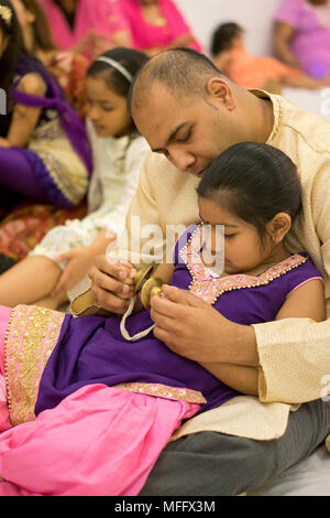 Ein Vater zu helfen ist meine Tochter spielen die Hand cymbals am Shri Lakshmi Narayan Mandir Tempel in Richmond Hill, Queens, New York. Stockfoto