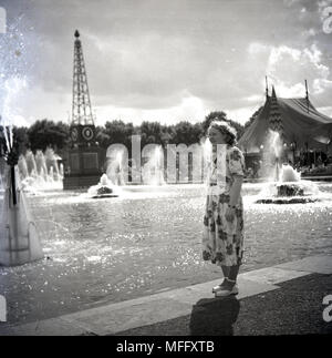 1951, historische, Dame in einem blümchenkleid stehend durch ein Display mit Springbrunnen auf dem Festival von Großbritannien, Battersea Park, London, England, UK. Die Idee, die hinter dem Festival feierte die britische Industrie, Kunst und Wissenschaft und inspirierende der Gedanke an eine bessere Großbritannien nach der Härte des post-ww2-Ära. Stockfoto