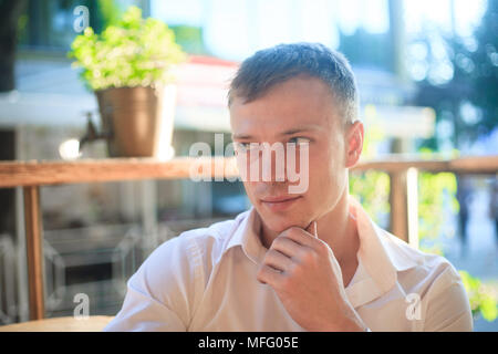 Eine junge, nachdenklich, stattlicher Mann in einem weißen Hemd im Freien. Stockfoto