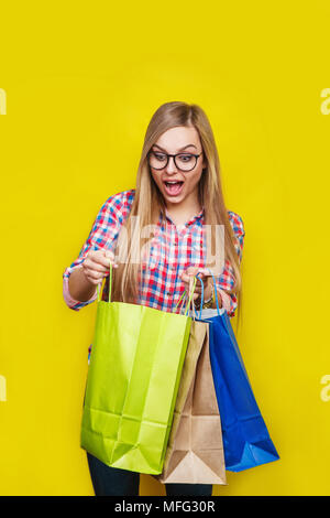 Nahaufnahme Porträt der jungen ziemlich überrascht, Frau mit Einkaufstüten, auf gelbem Hintergrund Stockfoto