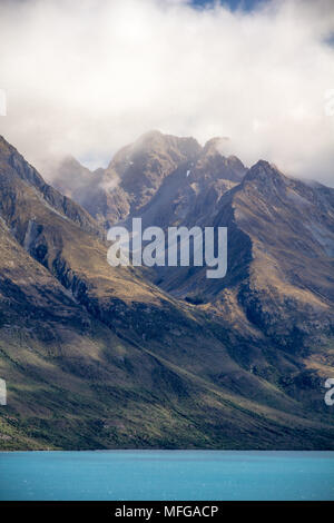 Dramatische Berge ragen steil aus dem türkisfarbenen Wasser des Lake Wakatipu in Neuseeland. Nach den jüngsten Regen, Nebel hängt noch um gezackten Gipfeln. Stockfoto