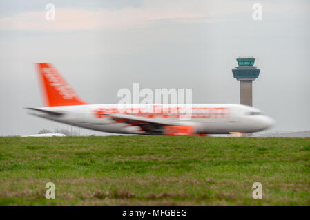 Eine kleine bis mittlere EasyJet Flugzeug Geschwindigkeiten entlang einer Start- und Landebahn mit Motion Blur vor der Air Traffic Control Tower am Flughafen Stansted Flughafen. Stockfoto