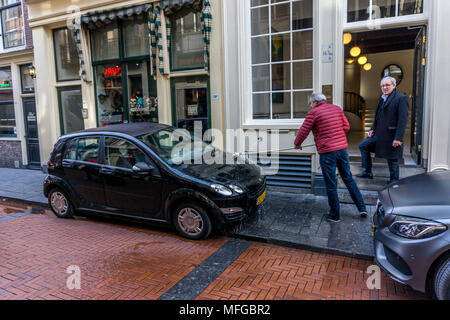 Ein Mann sein Auto Reinigung auf der Straße mit einem Pinsel auf Warmoesstraat, Amsterdam, Niederlande, Niederlande, Europa. Stockfoto