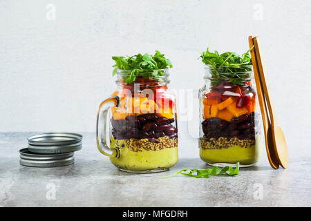 Regenbogenfarbige Salat in Gläsern auf dem Tisch. mit Bohnen, frischem Gemüse und Avocado Dressing mit Limettensaft und Senf. kopieren. Stockfoto