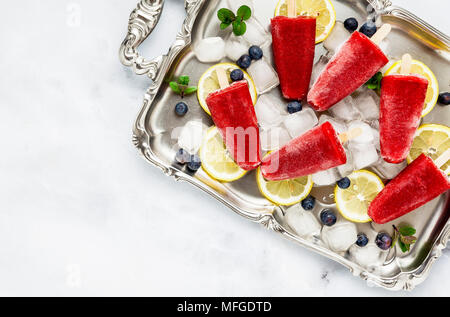 Frozen strawberry Saft Snack Eis pop oder popsicle auf weißem Marmortisch mit Heidelbeeren und Eis mit Minze. Sommer Eis frische Lebensmittel Hintergrund Stockfoto