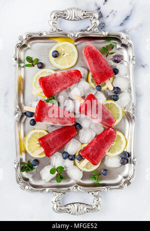 Frozen strawberry Saft Snack Eis pop oder popsicle auf weißem Marmortisch mit Heidelbeeren und Eis mit Minze. Sommer Eis frische Lebensmittel Hintergrund Stockfoto