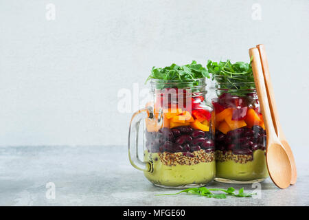 Regenbogenfarbige Salat in Gläsern auf dem Tisch. mit Bohnen, frischem Gemüse und Avocado Dressing mit Limettensaft und Senf. kopieren. Stockfoto