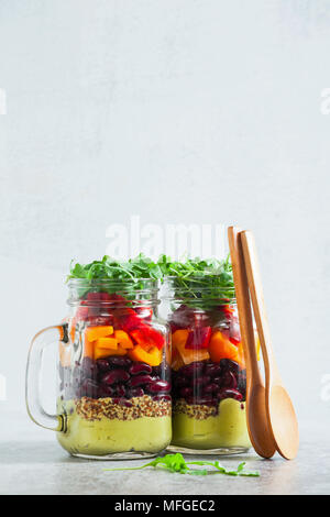 Regenbogenfarbige Salat in Gläsern auf dem Tisch. mit Bohnen, frischem Gemüse und Avocado Dressing mit Limettensaft und Senf. kopieren. Stockfoto