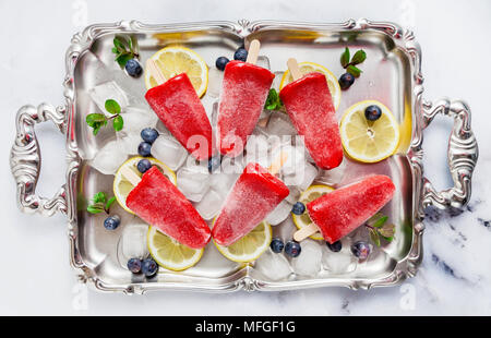 Frozen strawberry Saft Snack Eis pop oder popsicle auf weißem Marmortisch mit Heidelbeeren und Eis mit Minze. Sommer Eis frische Lebensmittel Hintergrund Stockfoto