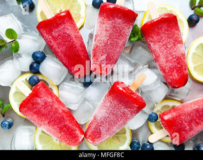 Frozen strawberry Saft Snack Eis pop oder popsicle auf weißem Marmortisch mit Heidelbeeren und Eis mit Minze. Sommer Eis frische Lebensmittel Hintergrund Stockfoto