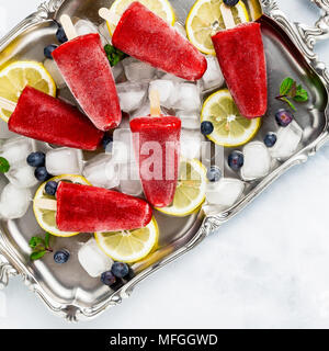 Frozen strawberry Saft Snack Eis pop oder popsicle auf weißem Marmortisch mit Heidelbeeren und Eis mit Minze. Sommer Eis frische Lebensmittel Hintergrund Stockfoto