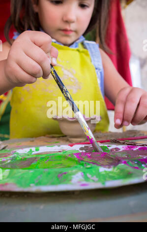 Kind Mädchen laden mit brauner Farbe ihre Bürste. Keramische Werkstatt für Kinder Konzept Stockfoto