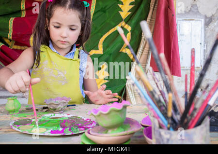 Kind Mädchen laden mit gelber Farbe ihre Bürste. Keramische Werkstatt für Kinder Konzept Stockfoto