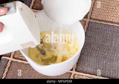 Das Mischen von Butter mit Zucker in weiße Schüssel zum Backen von Kuchen. Am Tisch als Hintergrund. Stockfoto
