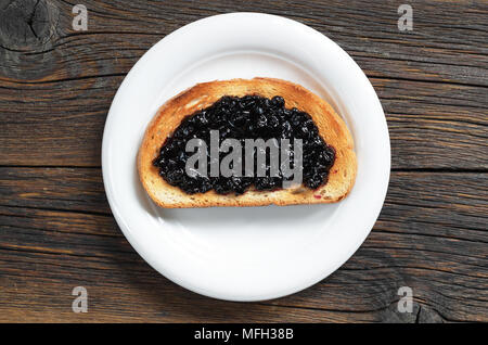 Geröstetes Brot mit Blaubeer-marmelade in der Platte auf dem dunklen Holztisch, Ansicht von oben Stockfoto