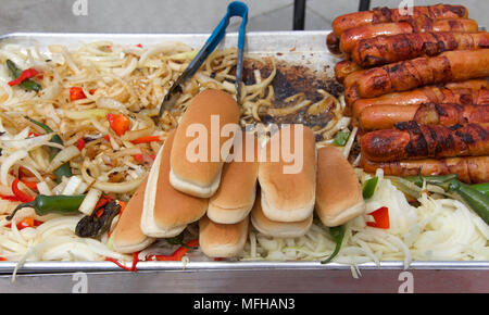 Hot dog street Hersteller Grill mit Speck umwickelt Hot Dogs, Zwiebeln, Pfeffer, Jalapenos auf eine dampfende Grill mit Zangen in Hintergrund und Hot Dog Buns. Pop Stockfoto