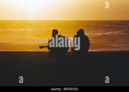 Silhouette der akustischen Gitarre spielen Musiker am Ocean Beach in San Francisco, Kalifornien bei Sonnenuntergang. Stockfoto