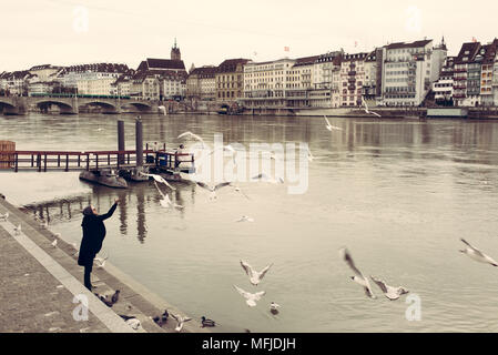 Hipster Mann füttern Möwen auf Basel riverfront gegenüber der Basler Altstadt (Altstadt) auf den Fußweg entlang des Rheins. Stockfoto