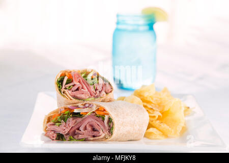 Ein schinkensandwich Wrap mit Salat, Karotten und Chips in einem Restaurant. Stockfoto