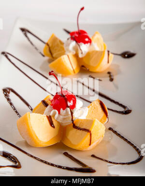 Eine Platte mit zwei Portionen Mango Mochi Eis mit Sahne und Kirschen. Stockfoto