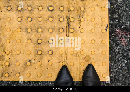 Zwei spitze Stiefel stehend auf eine gelbe Bürgersteig Sicherheitsrost Stockfoto